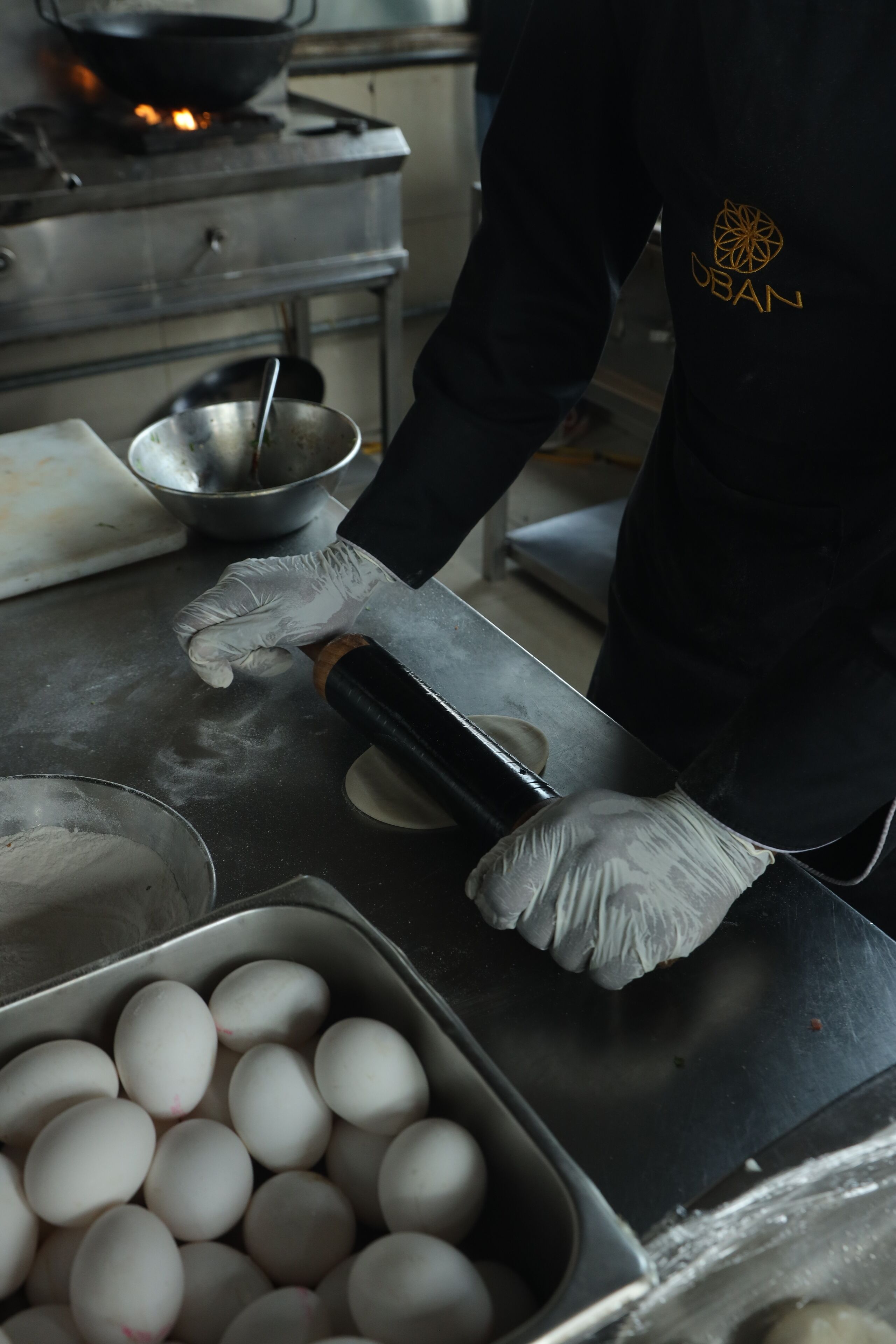 Una persona con grembiule e guanti neri maneggia delle uova su un bancone in acciaio inox.
