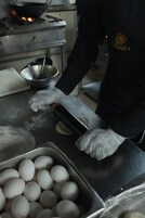 Una persona con grembiule e guanti neri maneggia delle uova su un bancone in acciaio inox.