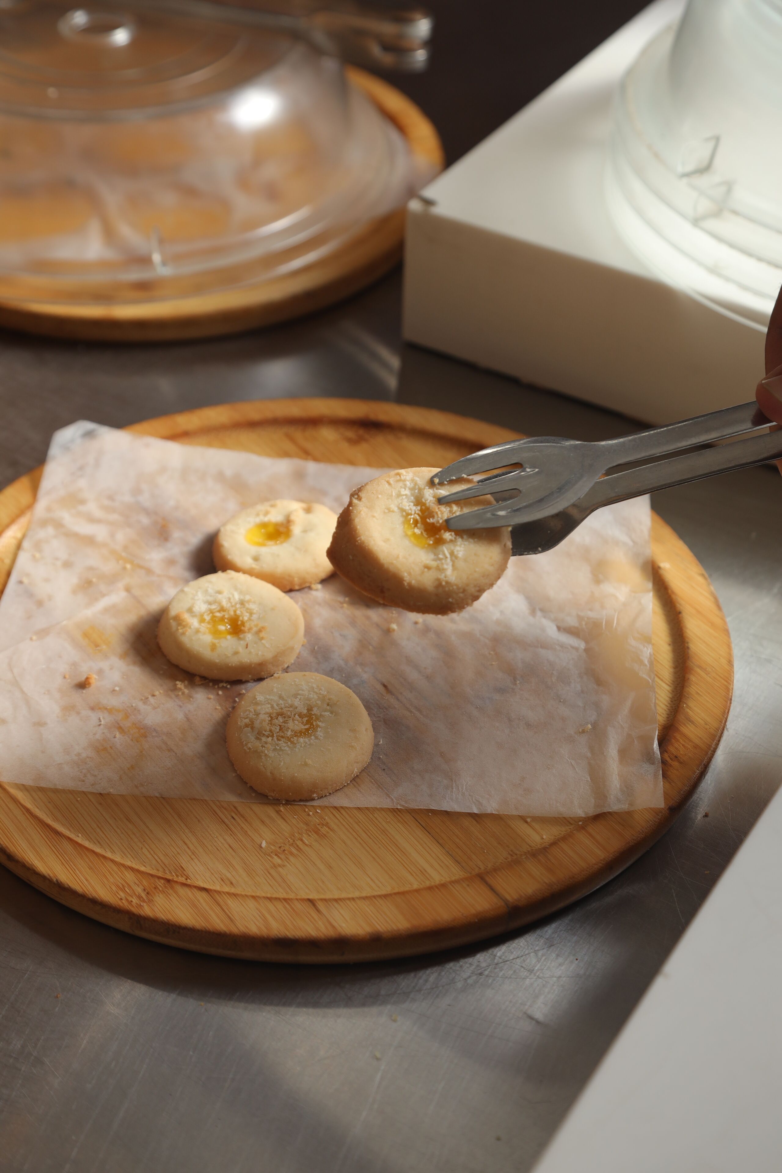 A wooden cutting board with a piece of parchment paper, a metal fork, and a covered container in the background.