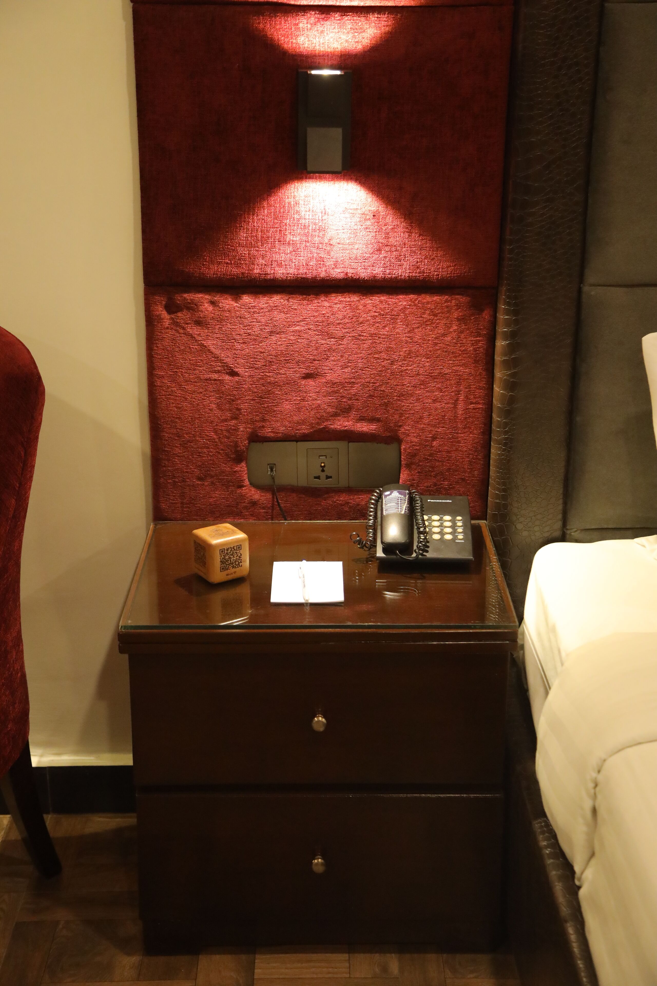 Una mesita de noche de madera con un teléfono, un código QR y una cajita.