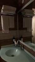 Une salle de bain avec un mur en bois, un grand miroir et un lavabo avec un flacon de savon pour les mains.