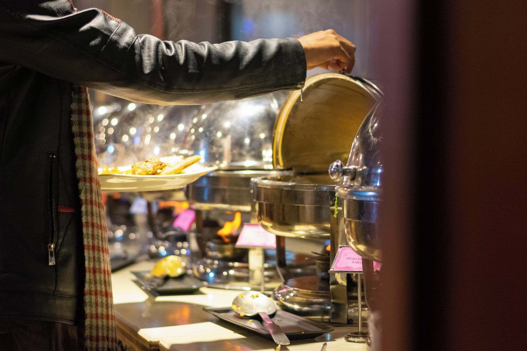 Une personne servant des plats provenant d’un buffet, en utilisant une louche et un plateau.