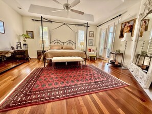 Ein geräumiges Schlafzimmer mit einem großen Bett, einem Baldachin, einem roten Teppich mit Muster und einem Deckenventilator.