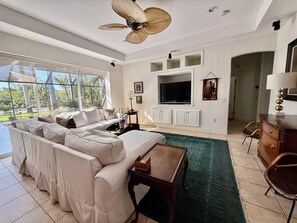 Ein geräumiges Wohnzimmer mit einer großen Couch, einem Fernseher und einem Deckenventilator.