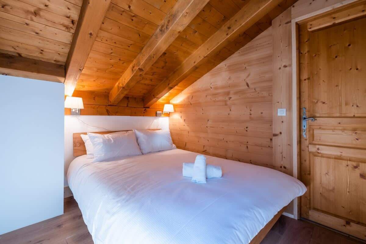 Une pièce aux murs lambrés, avec un lit, deux lampes de chevet et une porte en bois.