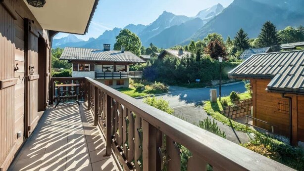 A balcony with a view of a mountain landscape, wooden buildings, and a clear sky.