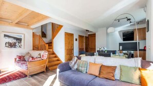 A cozy living room with a sofa, a wooden staircase, and a kitchen area.