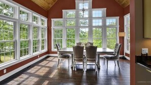 A dining area with a large table and chairs, surrounded by large windows with multiple panes. - Peaceful Mountain Oasis (Woodstock)