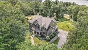 A large, two-story house with a prominent front porch, surrounded by dense forest and a lake in the background. - Peaceful Mountain Oasis (Woodstock)