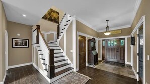 A spacious foyer with a wooden staircase, a large rug, and a chandelier. - Peaceful Mountain Oasis (Woodstock)