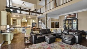 A spacious living area with a large sectional sofa, a kitchen in the background, and a staircase leading to an upper level. - Peaceful Mountain Oasis (Woodstock)