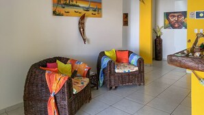 A living room with wicker furniture, colorful cushions, and a painting of a beach scene. - Pousada A Praia (Parnamirim)