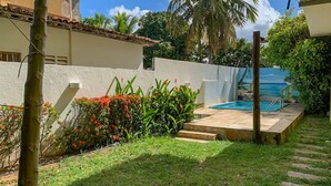 A pool area with a clear view of the ocean, surrounded by lush greenery and a white building with a tiled roof. - Pousada A Praia (Parnamirim)