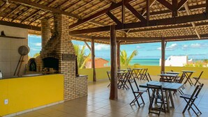 A covered outdoor dining area with brick walls, a brick fireplace, and a view of the ocean. - Pousada A Praia (Parnamirim)
