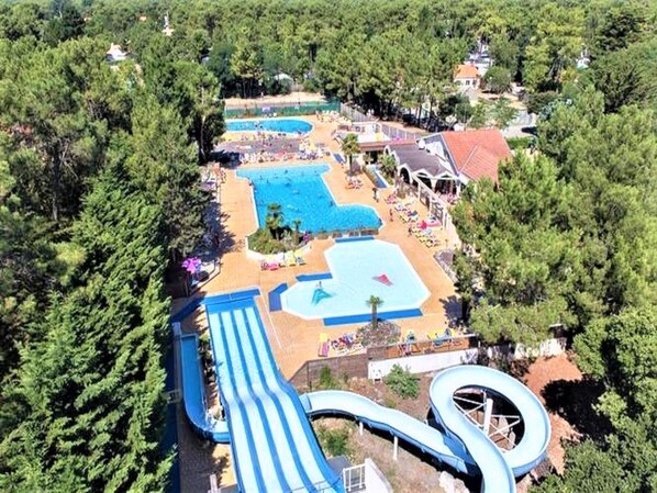 An aerial view of a resort with multiple swimming pools, a water slide, and lounge areas surrounded by dense trees.