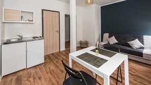 A compact living space with a kitchenette, a dining area with a table and chairs, and a dark-colored sofa with cushions. - Pension Michelangelo (Eisenach)