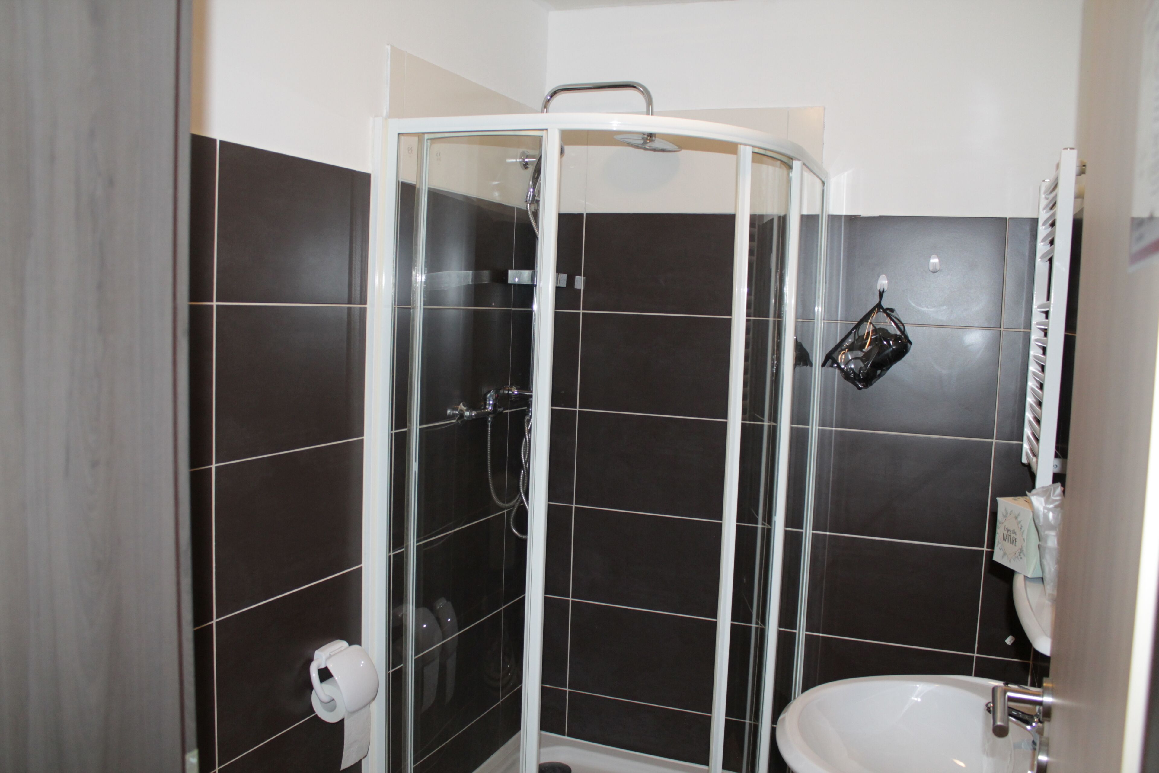 Un baño con ducha vidriada, lavamanos blanco y paredes de azulejos oscuros.