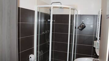 Un baño con ducha vidriada, lavamanos blanco y paredes de azulejos oscuros.