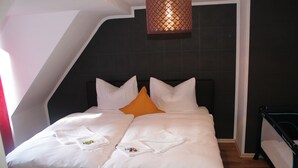 A neatly made bed with white linens and an orange pillow, a black headboard, and a hanging light fixture. - Pension Michelangelo (Eisenach)
