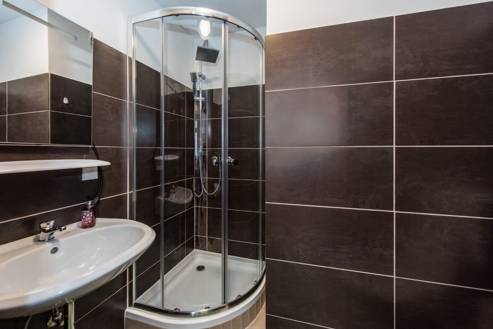 A modern bathroom with a glass-enclosed shower, a white sink, and dark brown tiles.