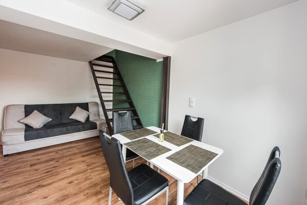 A compact living space with a dining area, a sofa, a staircase, and a green accent wall. - Pension Michelangelo (Eisenach)