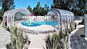 Una piscina con dos zonas cubiertas, rodeada de plantas y árboles.