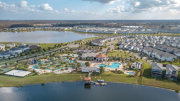 A residential area with multiple houses, a large swimming pool, and a lake.