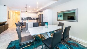 A modern kitchen with white cabinets, a stainless steel refrigerator, and a dining area with a white table and black chairs.