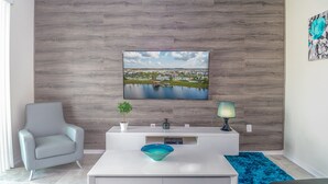 A modern living room with a white sofa, a coffee table with a blue bowl, a white console table with a lamp, and a large landscape painting on the wall.