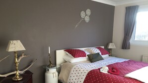Ein Schlafzimmer mit einem Bett, einem Nachttisch mit Lampe, einer Wanddekoration und einem Fenster mit Vorhängen.