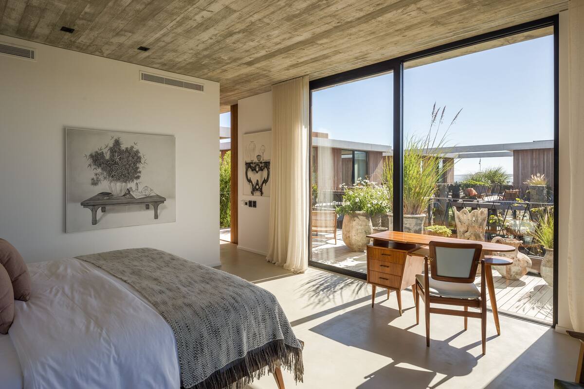 Un dormitorio con cama, escritorio y balcón con plantas en macetas.