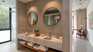 Un baño moderno con tocador de mármol, dos espejos redondos y estante de madera con toallas.