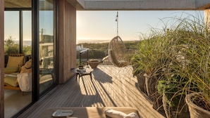 Un balcón moderno al aire libre con piso de madera, una silla colgante y plantas en macetas.