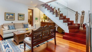 Ein modernes Wohnzimmer mit einer hölzernen Bank, einem Sofa und einer Treppe mit Holzstufen und einem Glasgeländer.