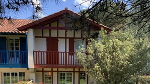 A two-story building with a red and white facade, a balcony, and a small garden area with a bench. - 3-room cottage near sea and golf in Moliets (Moliets-et-Maa)