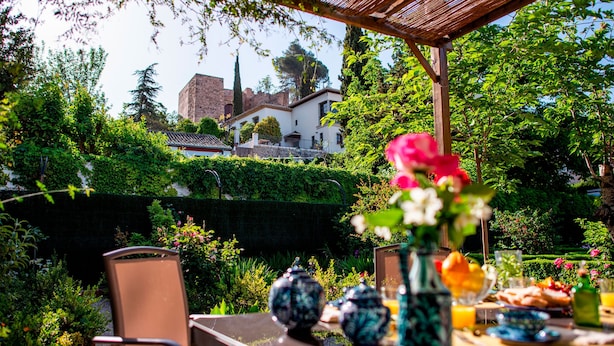 Ein Garten mit einer Terrassenfläche, einem für das Frühstück gedeckten Tisch, üppigem Grün und Blick auf ein historisches Gebäude.
