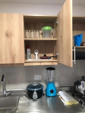 A kitchen with wooden cabinets, a sink, a stove, a blender, and a pot on the counter. - Apartahotel Zeus (Medellín)