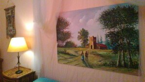 A room with a painting of a rural landscape, a lamp on a side table, and a wall hanging. - Palermo Centrale (Palermo)