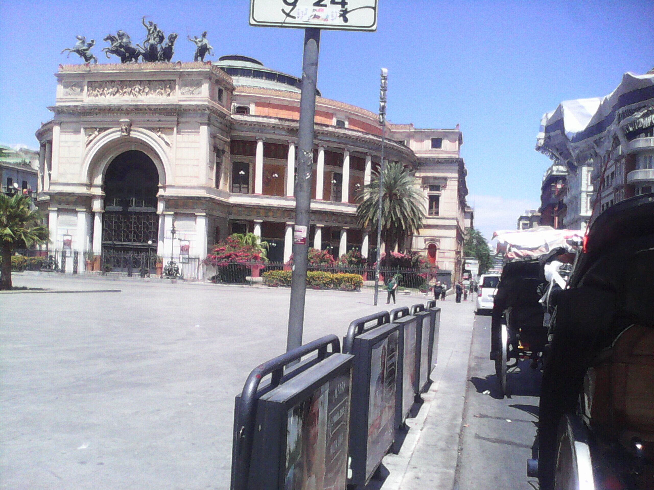 A street with a large, ornate building featuring an arched entrance and statues on top.