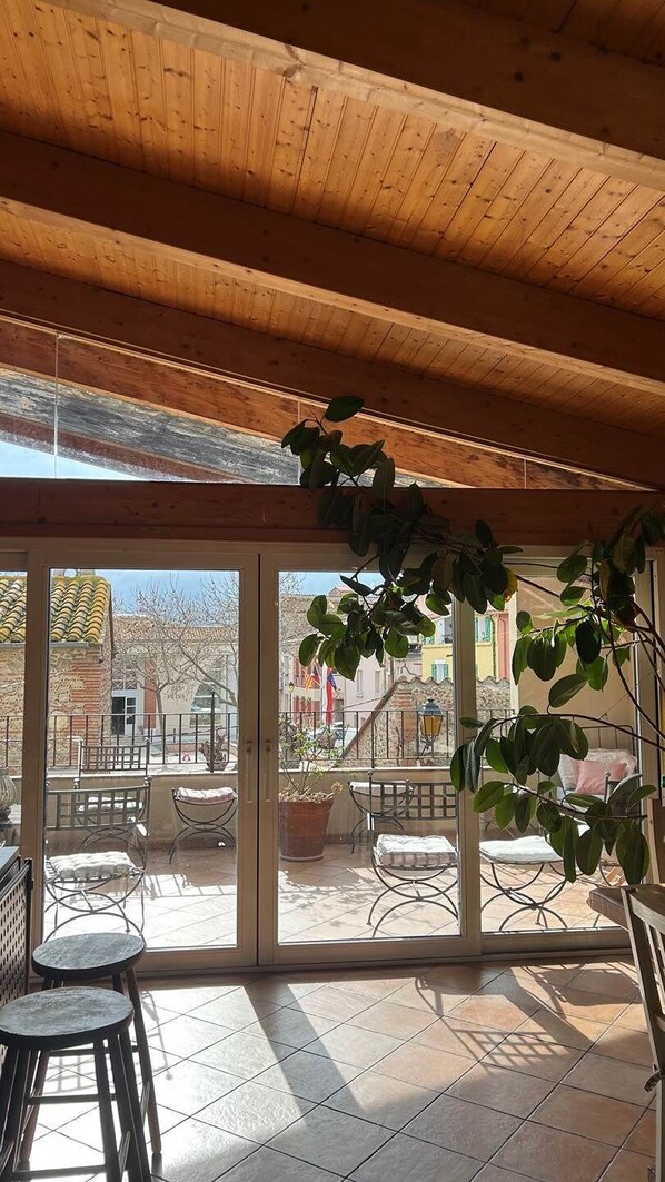 A covered patio with a view of a residential area, featuring a wooden ceiling, large sliding glass doors, and outdoor furniture. - Country house with a lot of character in Corneilla del Vercol (CORNEILLA DEL VERCOL)