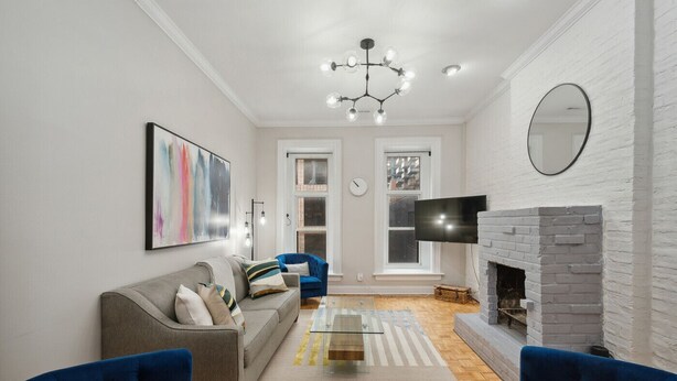 Een moderne woonkamer met een bank, blauwe stoelen, een open haard, een televisie en een groot abstract schilderij.