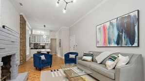 Een moderne woonkamer met een grijze bank, twee blauwe fauteuils, een glazen salontafel en een open haard.