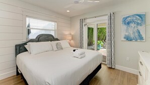 A bedroom with a bed, a ceiling fan, a window with blinds, a door leading to a balcony, and a painting on the wall. - Pineapple Cottage, tropical oasis pool/spa (Anna Maria)