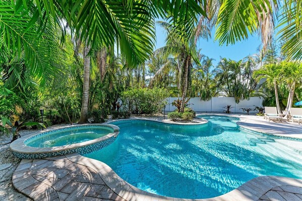 A swimming pool with a tiled edge, surrounded by palm trees and other greenery.