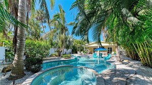 A pool area with two circular pools, surrounded by palm trees and a building with a yellow facade. - Pineapple Cottage, tropical oasis pool/spa (Anna Maria)