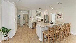 A modern kitchen with white cabinetry, a granite countertop, and a central island with wooden chairs. - Pineapple Cottage, tropical oasis pool/spa (Anna Maria)