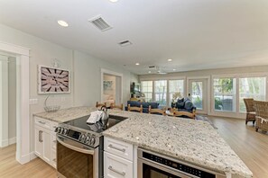 A modern kitchen with a central island, white cabinetry, and a dining area with a blue sofa and wicker chairs.