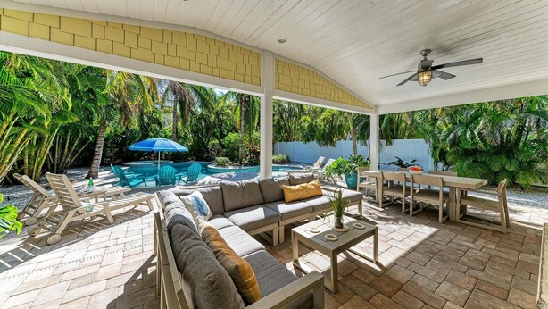 A covered outdoor patio with a pool, seating area, and lush greenery. - Pineapple Cottage, tropical oasis pool/spa (Anna Maria)