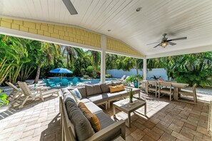 A covered outdoor patio with a pool, seating area, and lush greenery.
