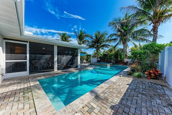 A swimming pool with a clear blue water, surrounded by palm trees and a covered patio area.